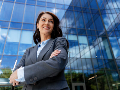 Businesswoman smiling with arms crossed in front of modern office building